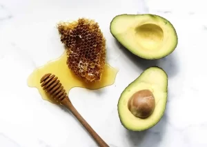 Avocado face mask for acne blended with honey in a small dish beside wooden spoon.