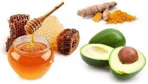 Golden turmeric stirred into avocado paste being applied to mature skin for anti-aging.