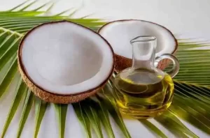 Glass bottle of coconut oil with fresh coconut halves.
