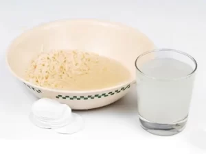 Woman applying a soaked cotton sheet mask to her face.
