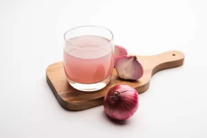 Fresh onion juice in a glass with red onions nearby.